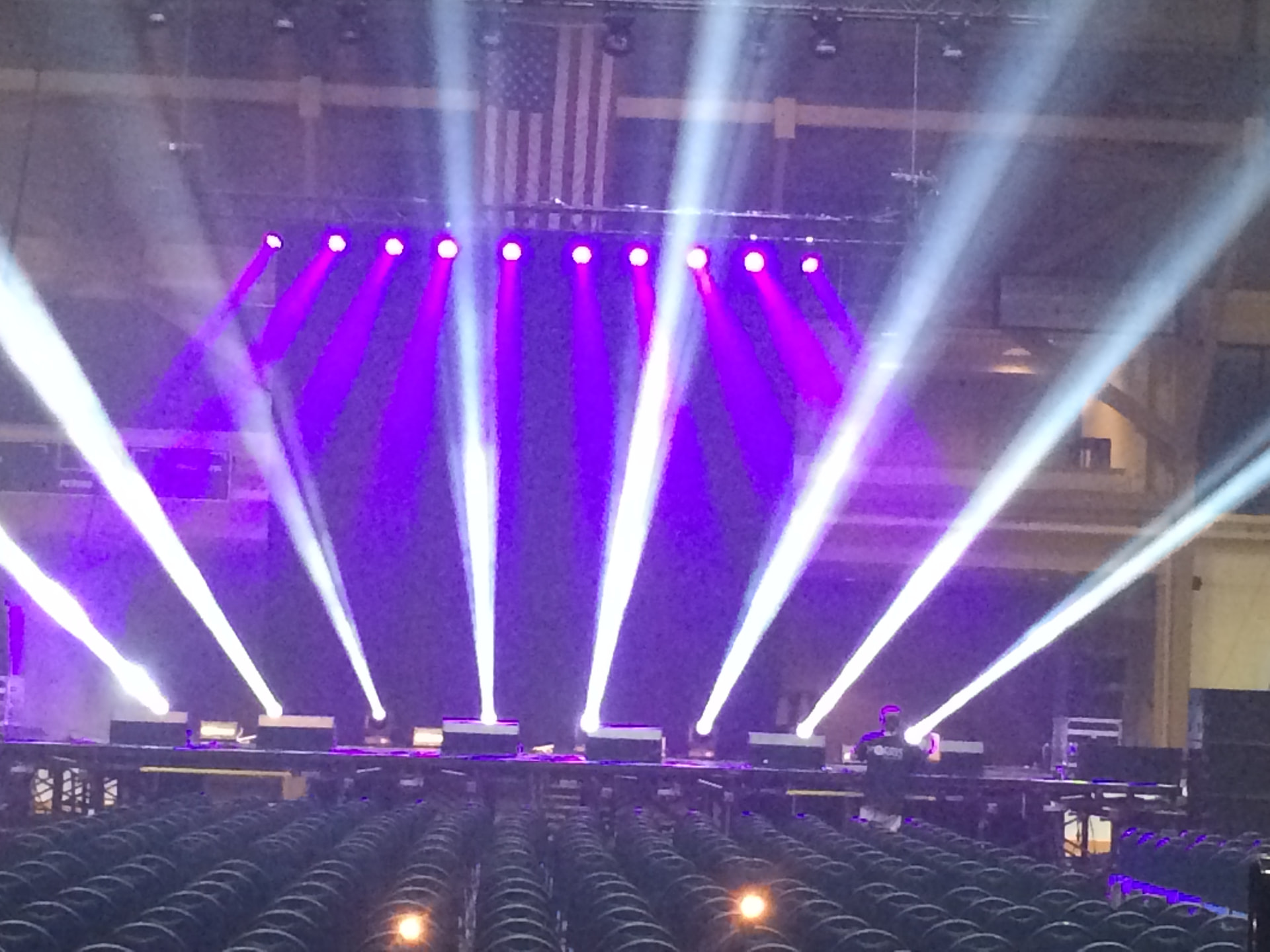 Fan of purple and white beam lights over an arena stage and audience seating