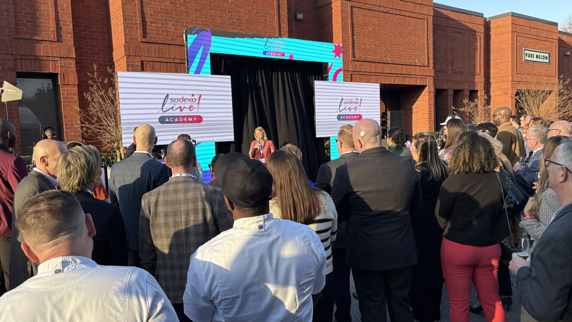 Outdoor Sodexo Live Academy event with LED screens, branded panels and a speaker addressing a crowd
