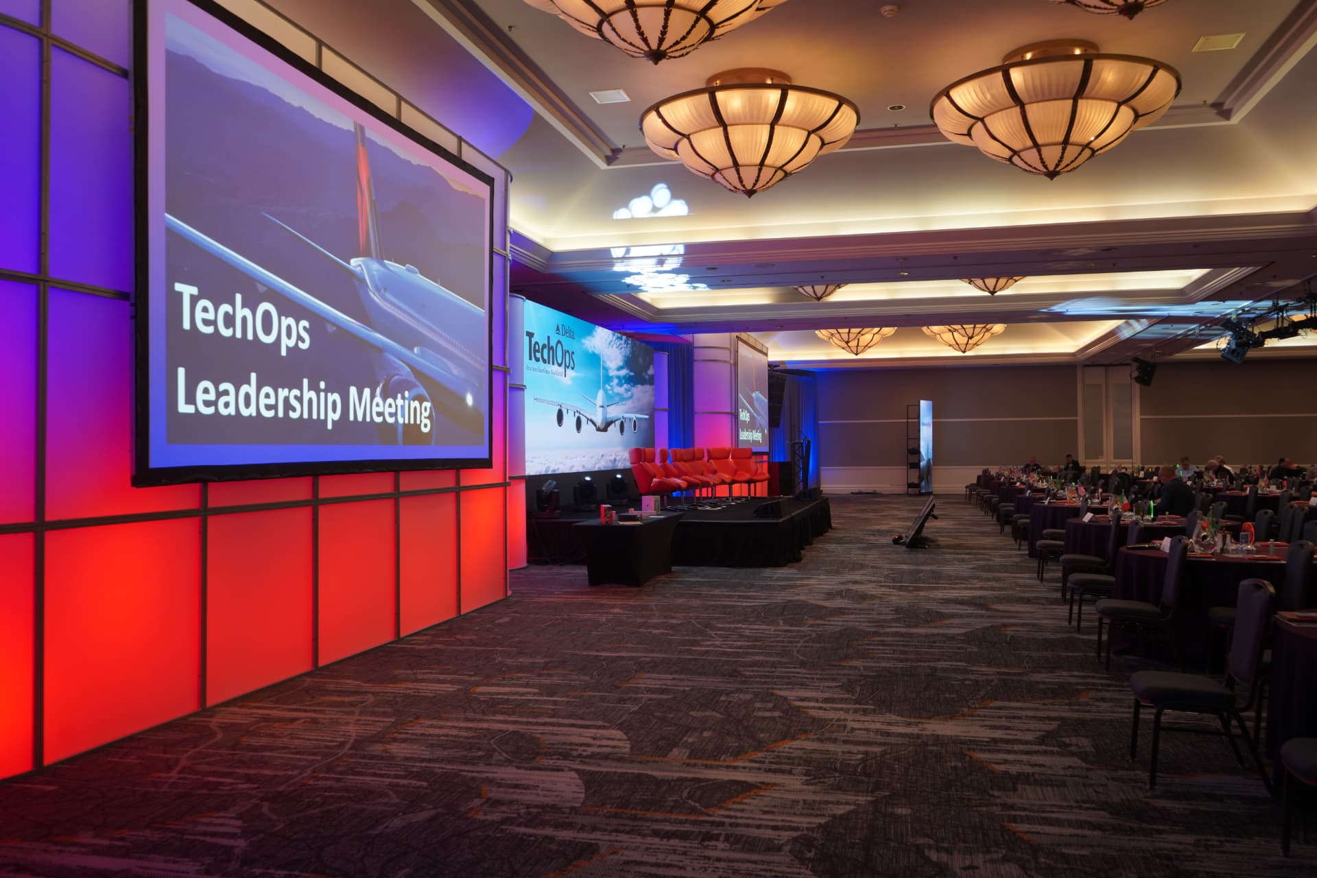 Corporate leadership meeting ballroom with projection screens, stage set and colored uplighting